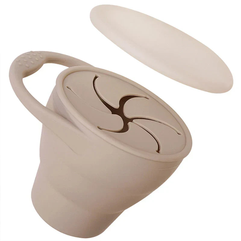 Green collapsible silicone food container next to a backpack, travel-friendly kids snack cup