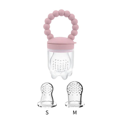 Baby gripping a yellow fruit feeder pacifier with fresh fruit pieces visible inside