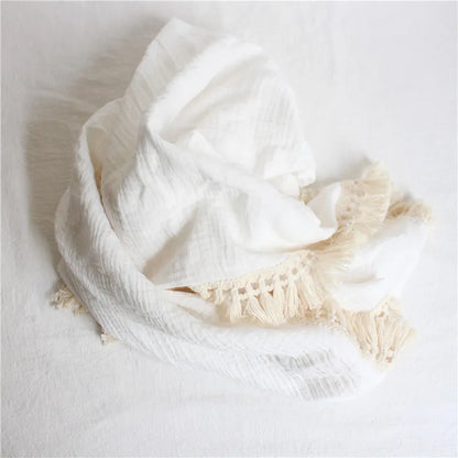 Close-up of soft cotton texture and tassel detail on a newborn swaddle blanket, baby comfort item