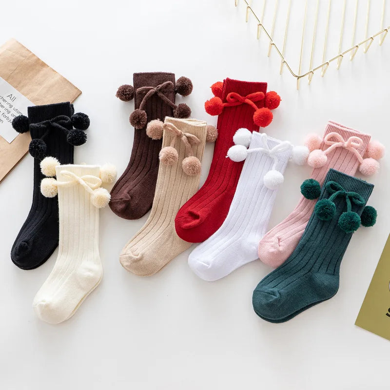 Pair of soft knit knee-high baby socks on a wooden background, natural feel.