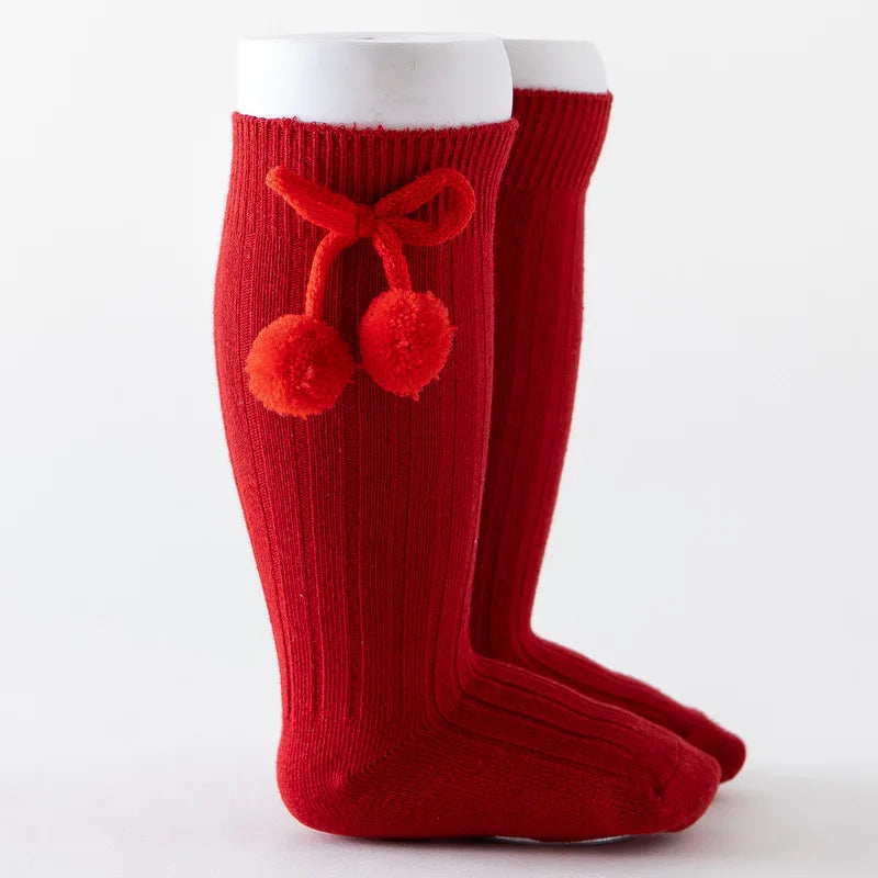Baby girl wearing pink soft knit knee-high socks, cozy & cute.