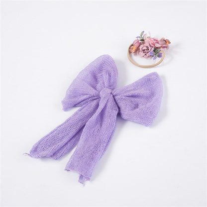 Newborn baby securely snuggled in a warm, cream-colored knitted mohair photography wrap and lace headband.