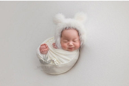 Baby photo shoot props with a soft gray swaddle blanket, matching hat, and tiny doll accessory.