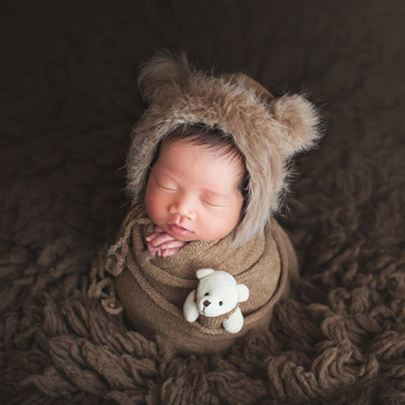 Newborn baby accessories: comfortable swaddle blanket, beanie hat, and doll for memorable photos.