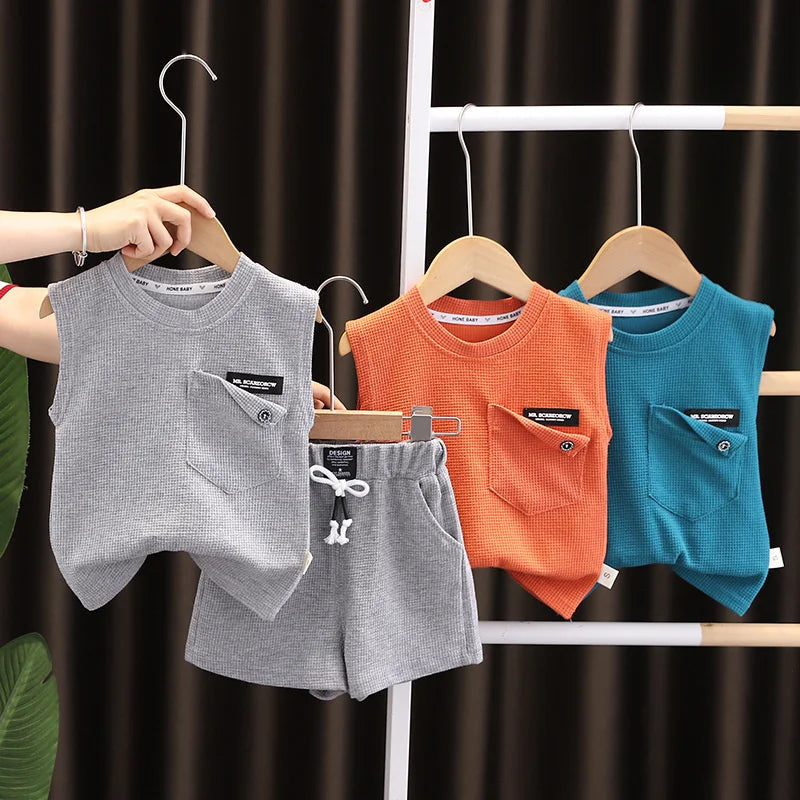 Toddler boy's summer sports outfit laid flat: blue sleeveless top and matching orange shorts, ready for play.