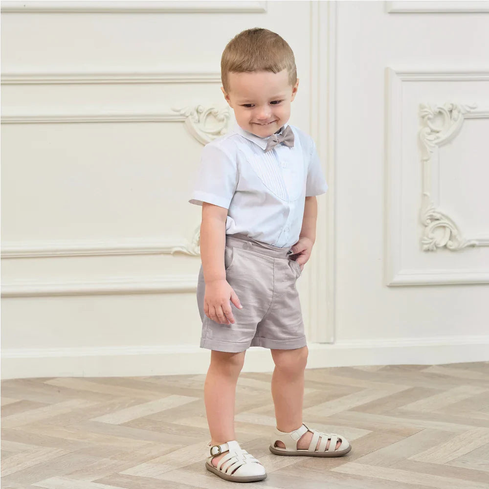 Full view of a toddler boy's summer party outfit: crisp cotton shorts, white shirt, suspenders, bow tie