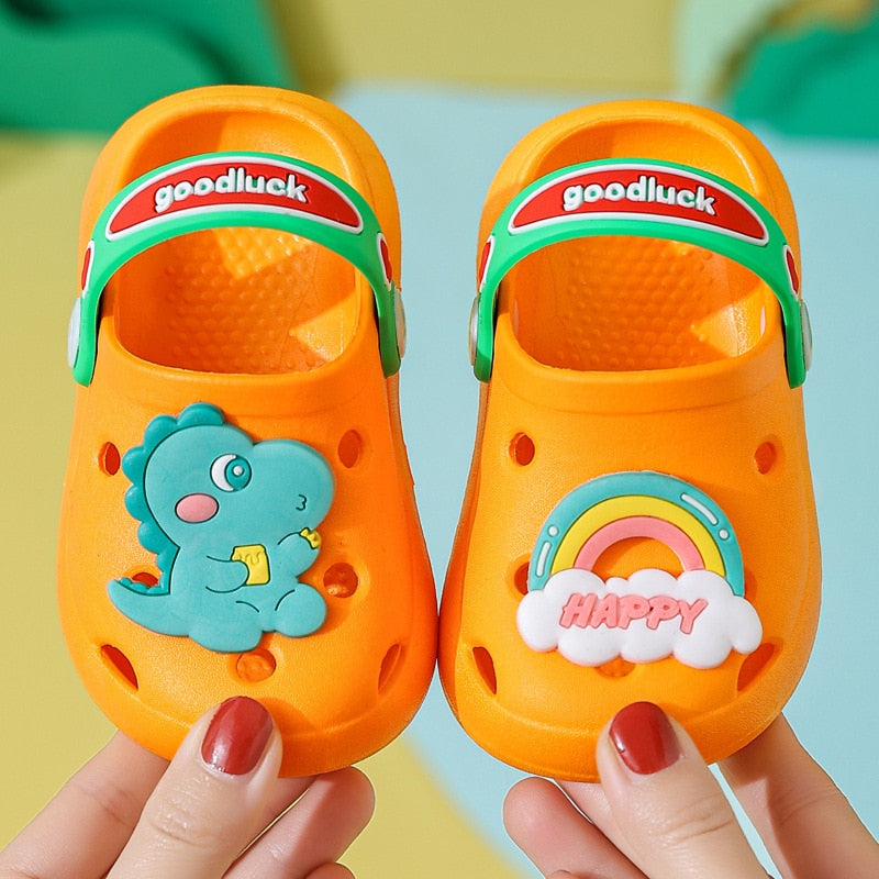 Happy toddler wearing blue dinosaur beach shoes, playing in sand