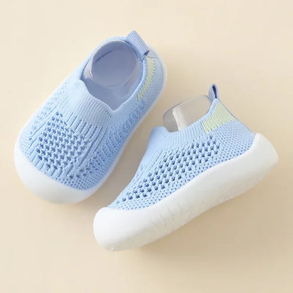 Infant wearing white soft sole sneakers, standing on a wooden floor