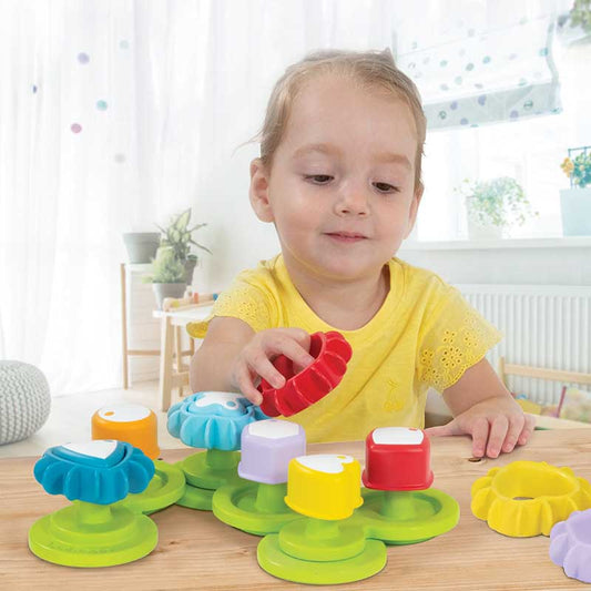 Toddler playing with multicolored shapes sorting gears toy on a natural wood floor, developing motor skills.