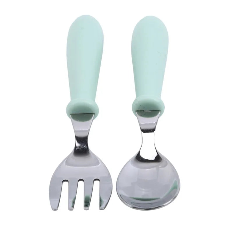 Cartoon stainless steel toddler dinnerware set arranged on a wooden table, featuring pink, blue & green pieces.
