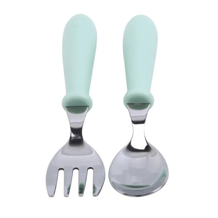 Cartoon stainless steel toddler dinnerware set arranged on a wooden table, featuring pink, blue & green pieces.