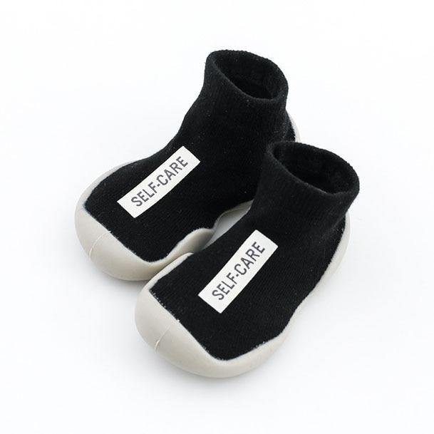 Front view of black soft-sole baby sock shoes, providing warmth and protection indoors