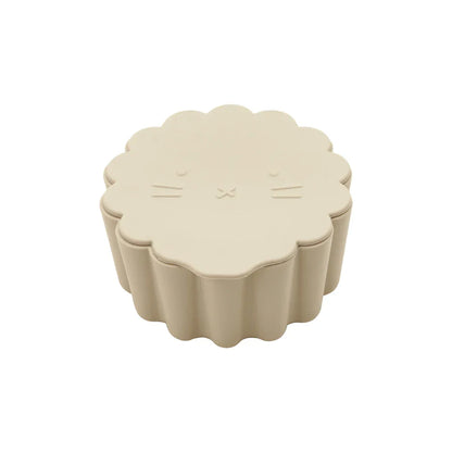Toddler reaching for snacks in a bright orange silicone cup with a funny cartoon face lid