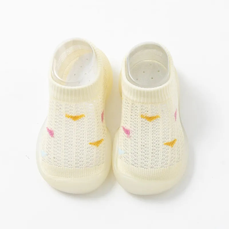 Baby's feet in pink soft sole non-slip walking shoes, standing on a rug.