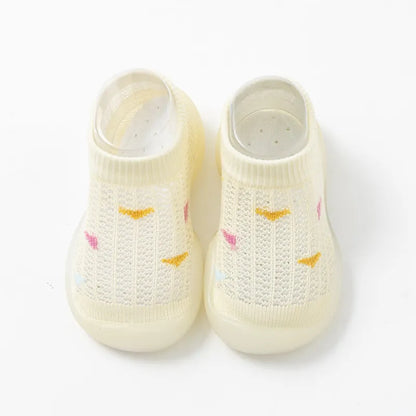 Baby's feet in pink soft sole non-slip walking shoes, standing on a rug.