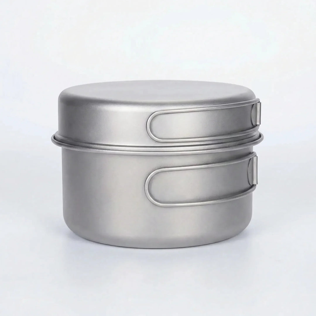 Compact titanium pot & pan set with folding handles, ideal for space-saving camping & outdoor cooking.