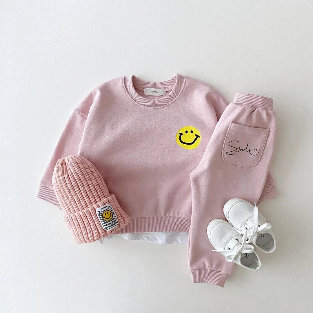 Toddler modeling a cozy yellow cotton smiley face tracksuit set, durable activewear for unisex babies.