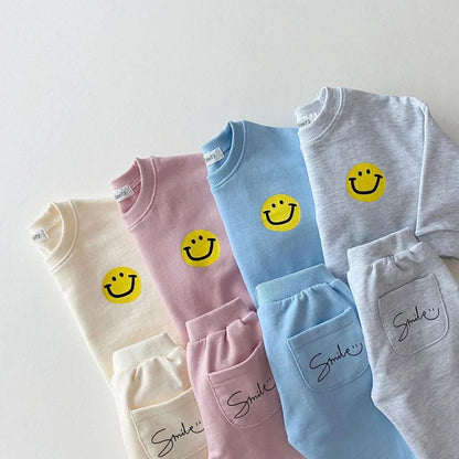 Adorable baby wearing a two-piece yellow cotton tracksuit set with cheerful smiley faces, infant activewear.