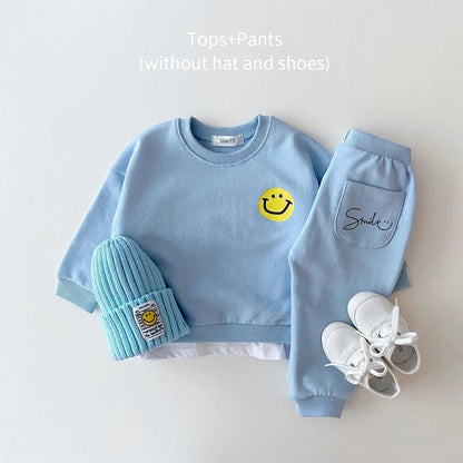 Side profile of a baby in a bright yellow cotton tracksuit with smiley face emblem, comfy infant apparel.