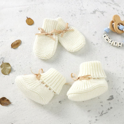 Unisex baby knitted set on a wooden surface, white booties, mittens, warm infant apparel gift