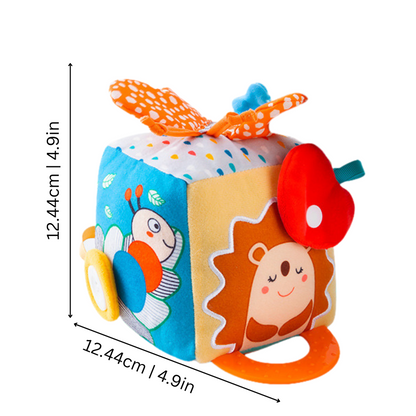 Infant exploring soft sensory cube with various tags & colors for early education, promoting developmental skills.