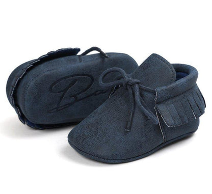 Baby's feet in brown faux suede unisex tassel moccasins, anti-slip first walker shoes.