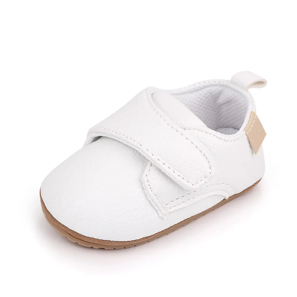 Adorable baby wearing classic red leather anti-slip first walker shoes, playing indoors