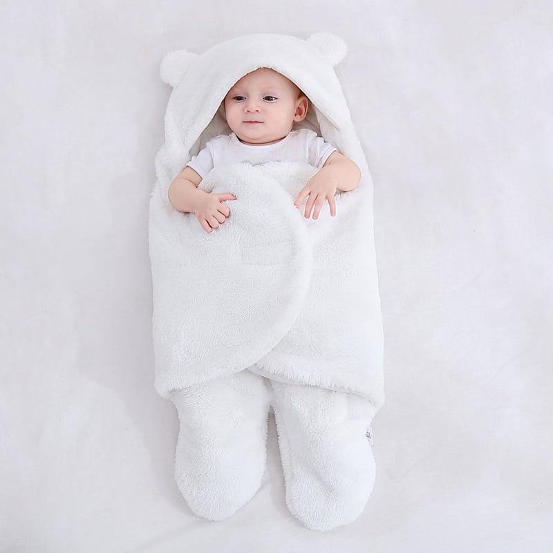 Newborn wrapped snugly in a cozy fleece bear ear swaddle blanket, peaceful sleep.