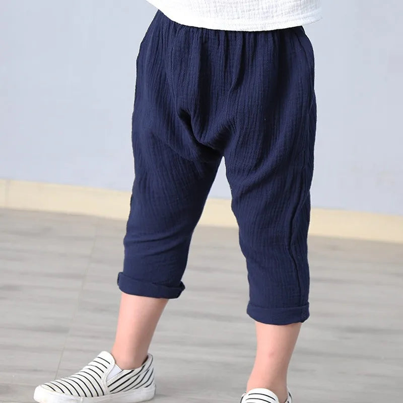 Stack of folded unisex kids' summer linen blend solid color pants in various colors