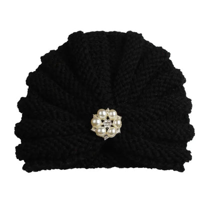 Smiling baby peeking over the top of a colorful knitted beanie, joyful winter hat