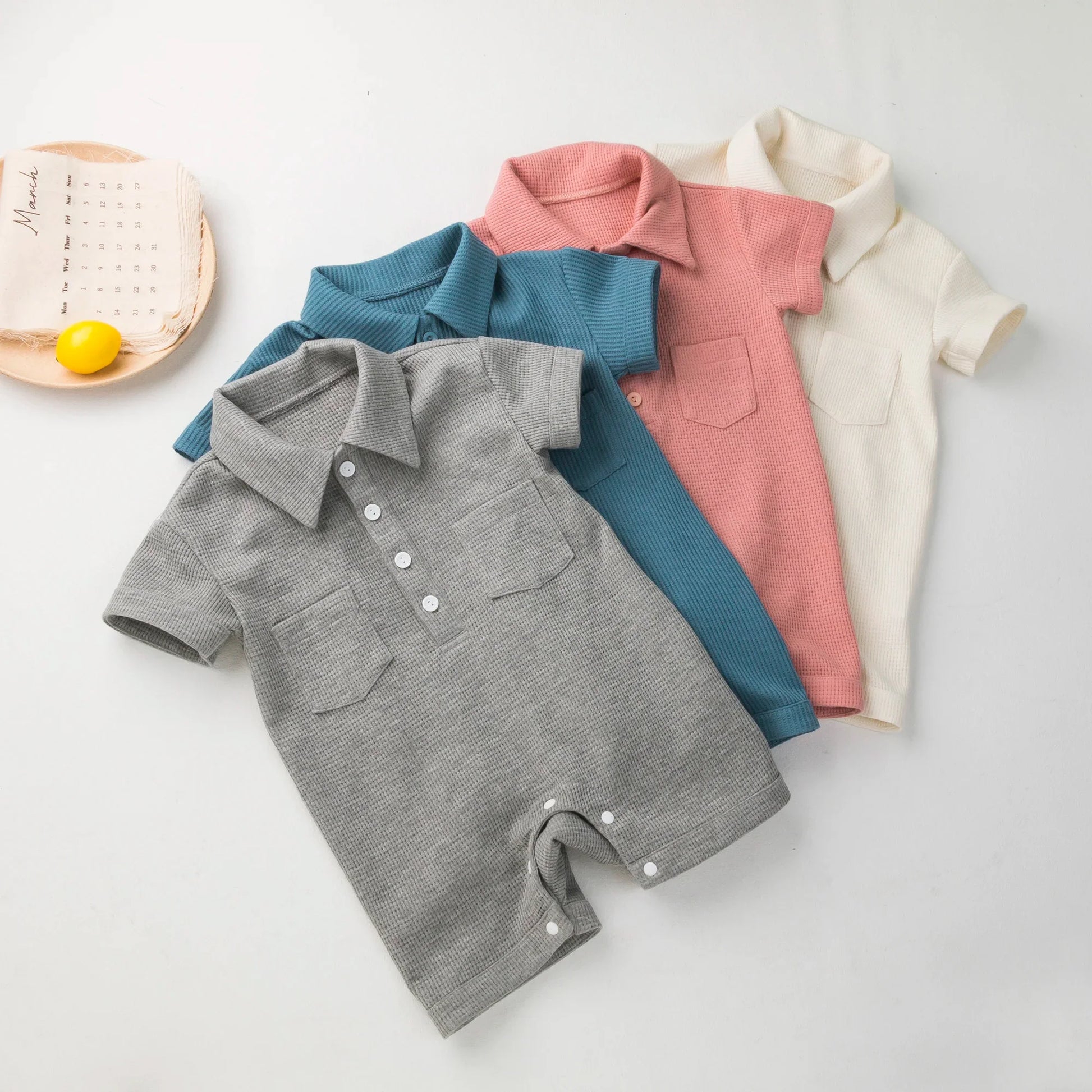 Display of various colored short sleeve baby jumpsuits on a rack.