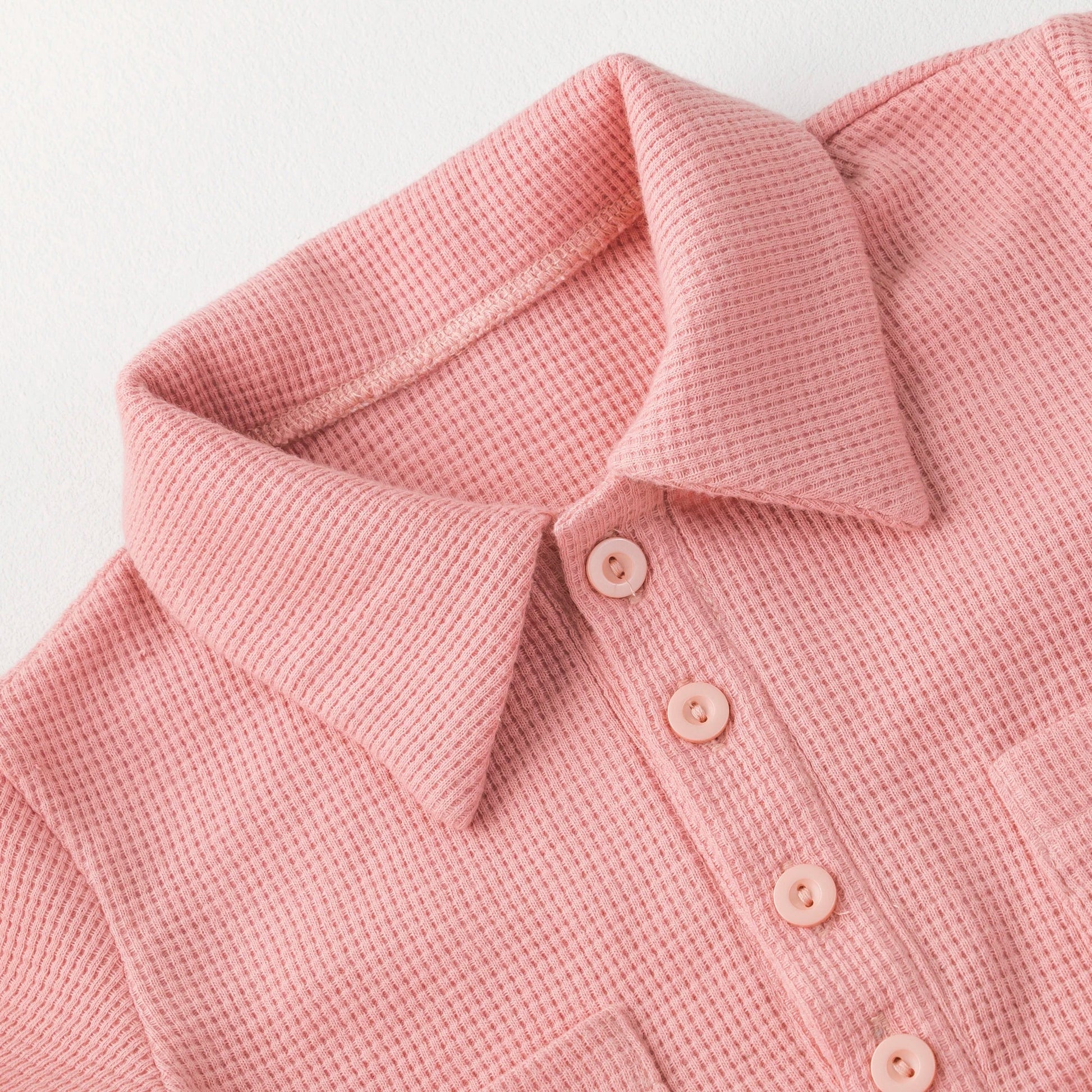 Close-up of a pink short sleeve cotton baby jumpsuit, soft fabric texture.