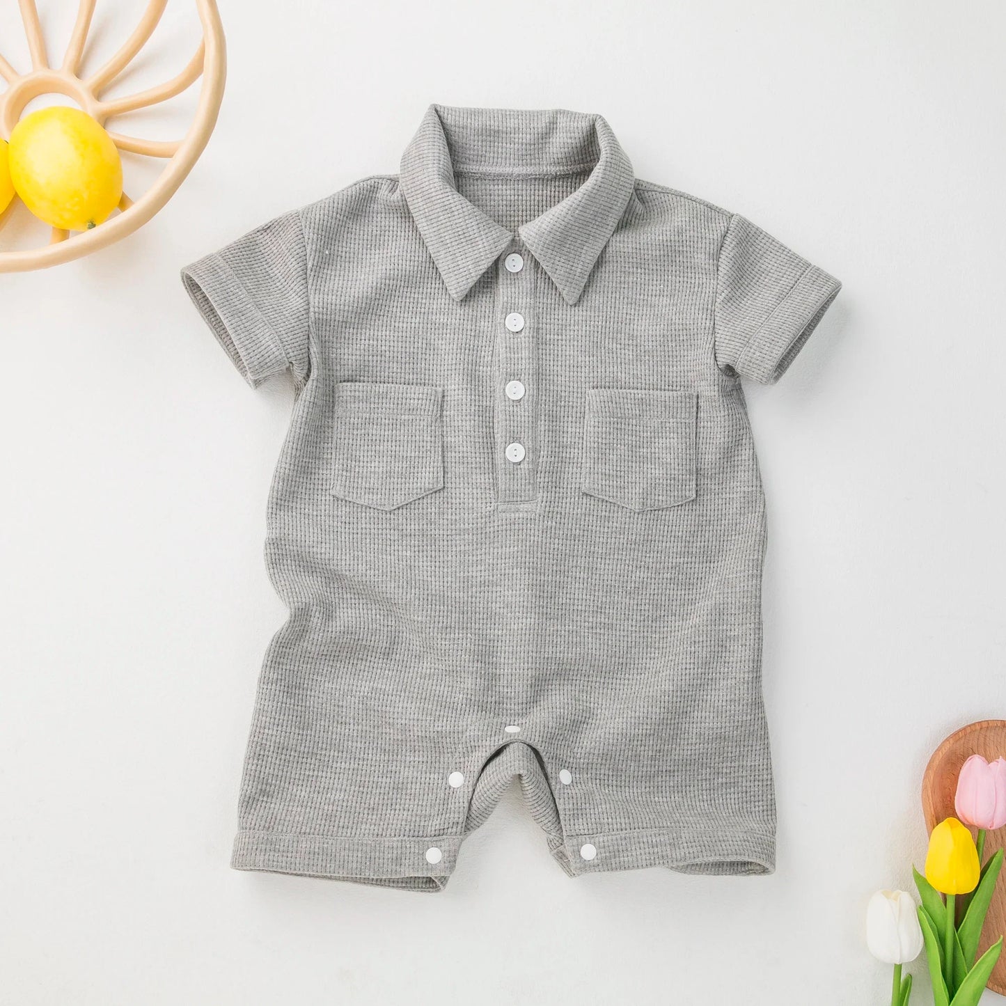 Baby in a grey short sleeve cotton jumpsuit, playing on a blanket.