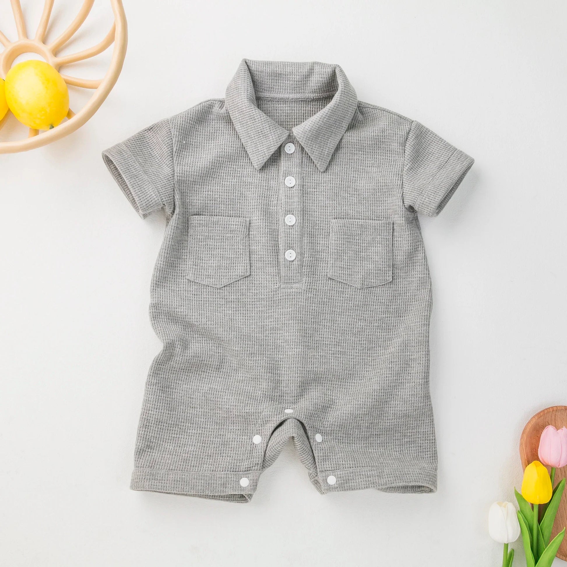 Baby in a grey short sleeve cotton jumpsuit, playing on a blanket.