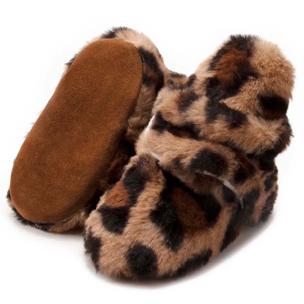 Hand holding a pair of soft fluff baby booties, unisex design, cozy first walkers for infants.