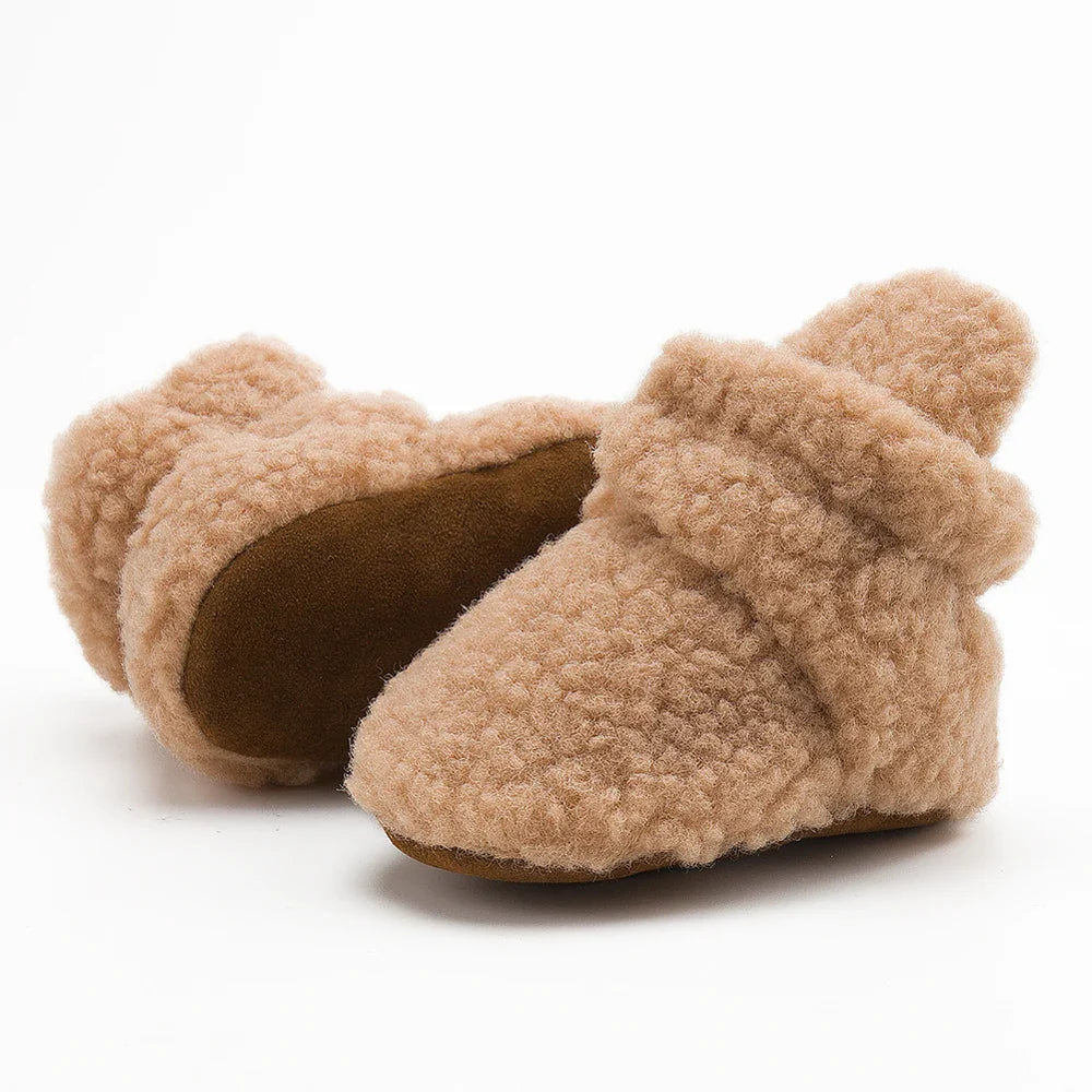 Pair of unisex soft fluff baby booties on a wooden floor, ready for infant's first steps.