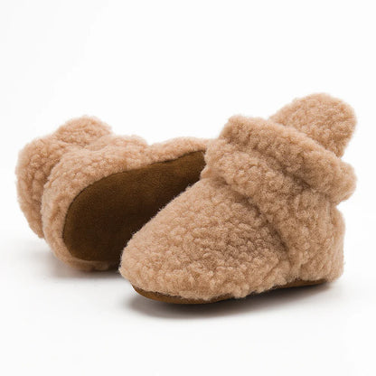 Pair of unisex soft fluff baby booties on a wooden floor, ready for infant's first steps.