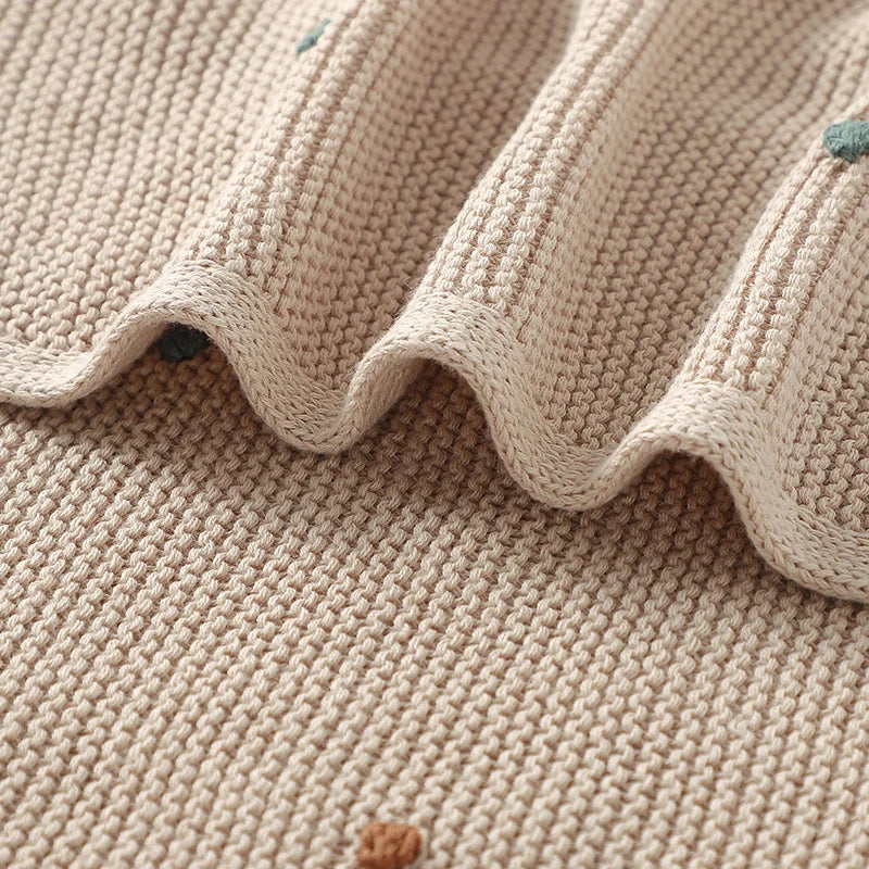 Folded cotton baby blanket in a neutral cream color, ideal unisex newborn essential and nursery decor