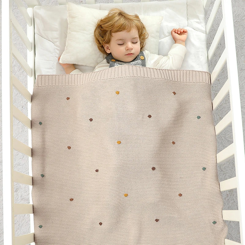 Stack of folded knitted baby blankets in various neutral colors, versatile for all season nursery decor