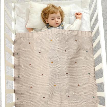 Stack of folded knitted baby blankets in various neutral colors, versatile for all season nursery decor