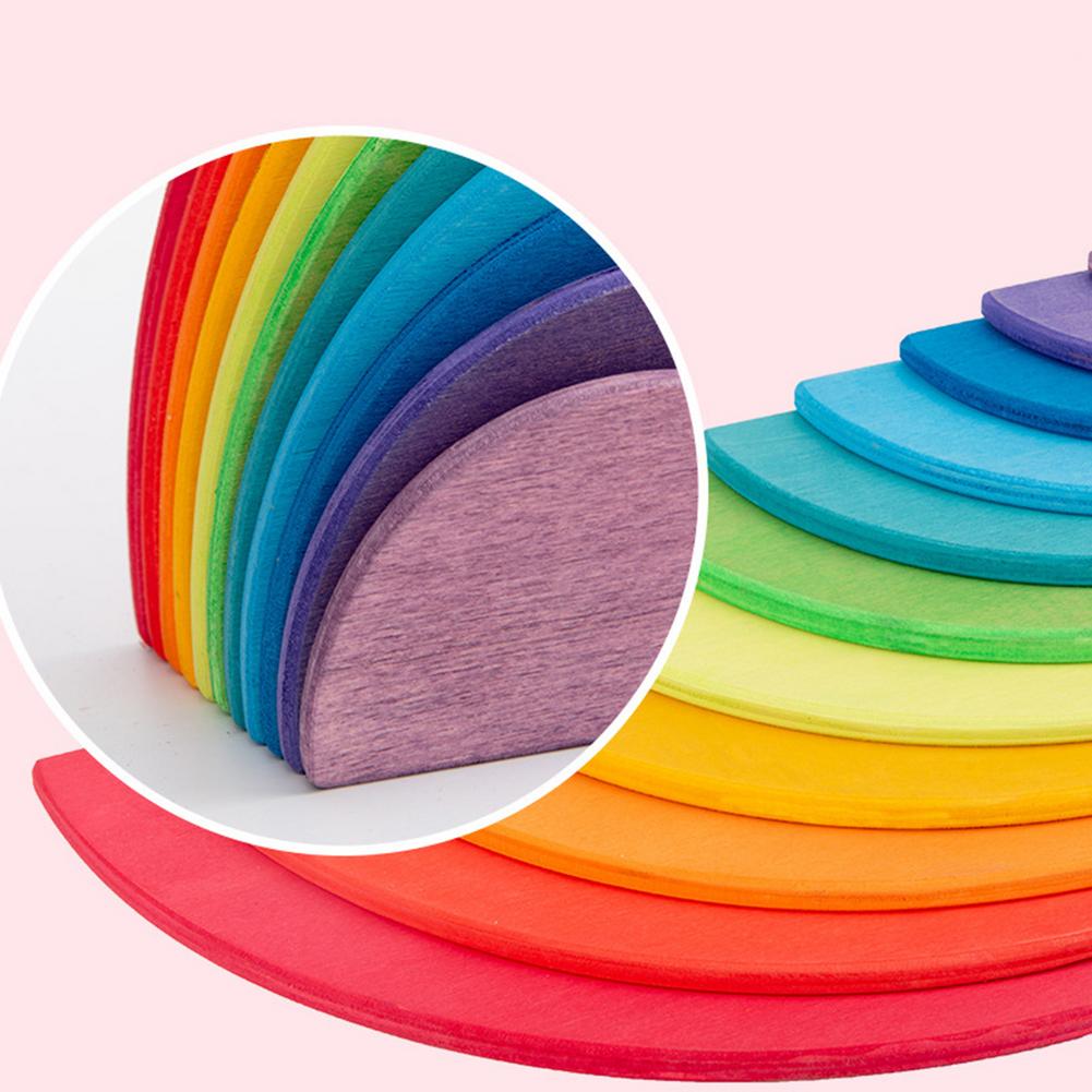 Child's hands stacking colorful wooden rainbow discs, promoting fine motor skills and creativity.