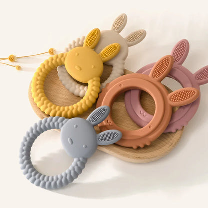 Baby holding an adorable pink rabbit silicone teether, safe and effective teething toy
