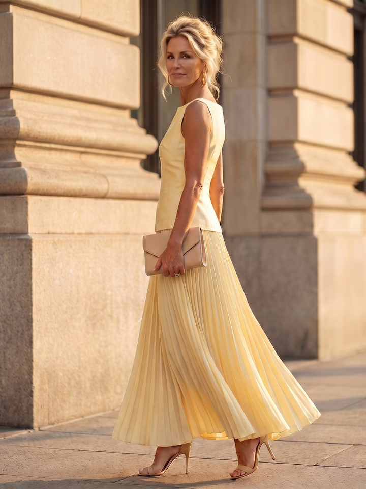 Stylish women's yellow pleated maxi skirt set with a structured sleeveless bodice for evening wear.