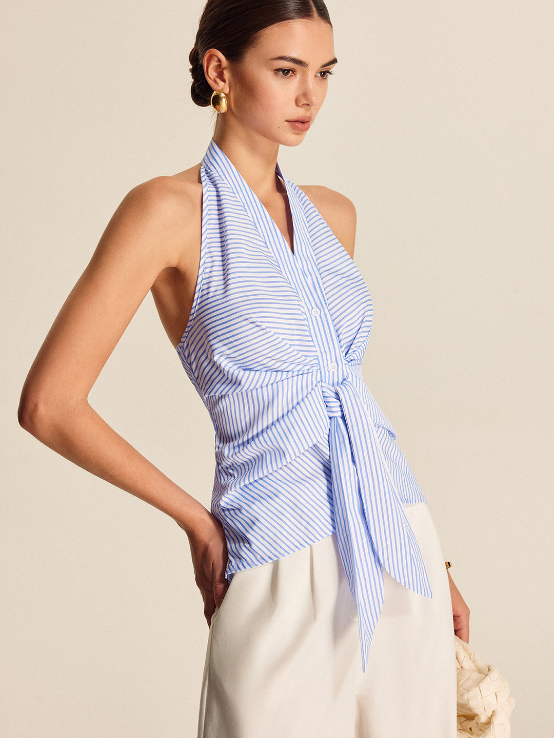 Elegant light blue striped women's blouse. Halter neck, tie-front, sleeveless design for versatile work fashion.