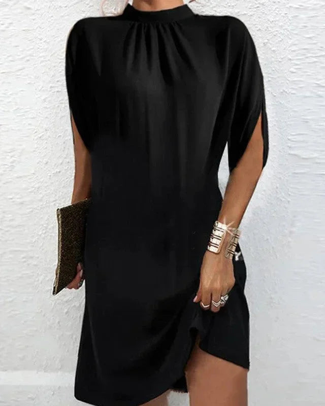Modern women's mini dress with mock neck, statement cape sleeves, and asymmetric hem detail.